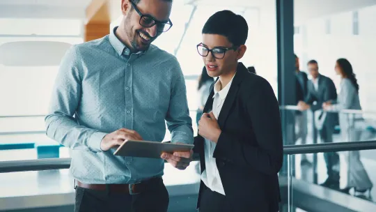 Dos compa帽eros de Gesti贸n Administrativa en una oficina analizan un proyecto en una tablet.