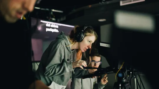 Operadora de cámara y otros técnicos graban una producción audiovisual.