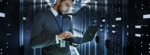 Informático en una sala de servidores, utiliza un portátil para configurar el sistema informático.