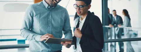 Dos compañeros de Gestión Administrativa en una oficina analizan un proyecto en una tablet.