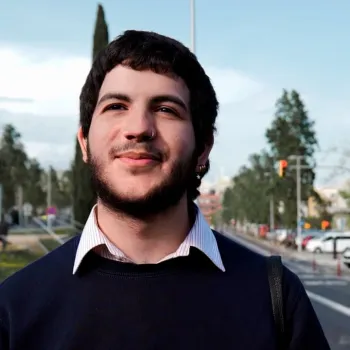 Hombre sonriendo en la calle mientras camina con camisa blanca y jersey azul