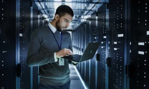 Informático en una sala de servidores, utiliza un portátil para configurar el sistema informático.