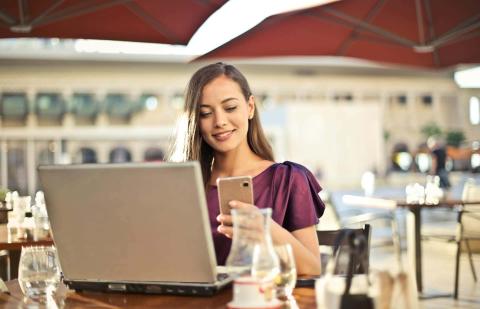 Una mujer navega por internet y usa el móvil en la terraza de un café.