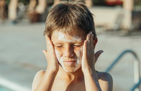 Niño echándose crema solar en la cara.