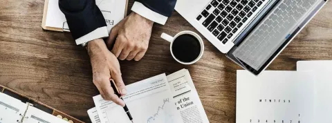 Un técnico en estudios de mercado expone su análisis con documentos y un portátil en una oficina.