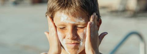 Niño echándose crema solar en la cara.