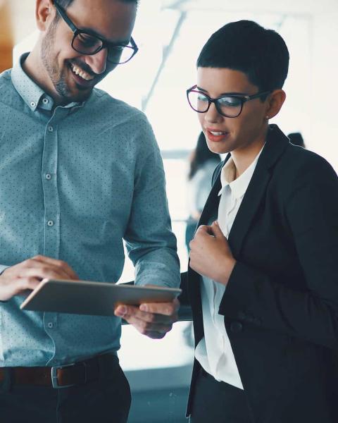 Dos compañeros de Gestión Administrativa en una oficina analizan un proyecto en una tablet.