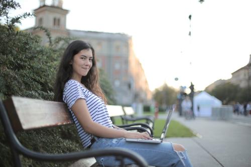 Una universitaria estudia en un banco en un parque con su portátil